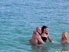 Two luscious babes (brunette and blond) hook up with a horny bald dude at they beach. They swim with him in the ocean wearing steamy bikini before he invites them over at his place.
