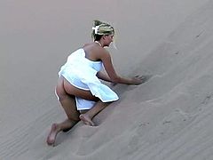 Sweet blonde babe in a white dress makes a solo show in the heart of a desert. She lies down on the sand. Her dress is flutters so that you can see her ass and pussy.