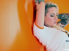 Christy Mack is wearing a regular top and posing in an orange room. She shows off her tattoos and she flashes her huge boobs as well. This is a sort of teaser.