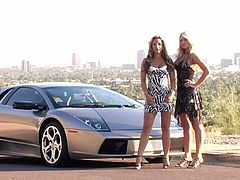 Two leggy babes in dresses show boobs near a sport car