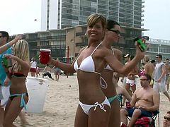 A huge crowd of people are having a praty at a beach. The girls, wearing sexy bikinis dance and shake their butts. Must-see action.