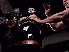 Dani is covered in latex; her face is nearly completely encased within the latex mask. One of the masters uses a torture device on her nipples. The powerful dominators slaps her big breasts and teach her how to have the best orgasm. She sits on the sybian; one of the masters controls the intensity.