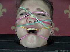 Ashley is tightly wedged in a single-board version of stocks. The topless beauty now has rubber bands stretched all over her face. She doesn't want one of those things to snap against her, so she keeps still, until the cattle prod zips her a little.